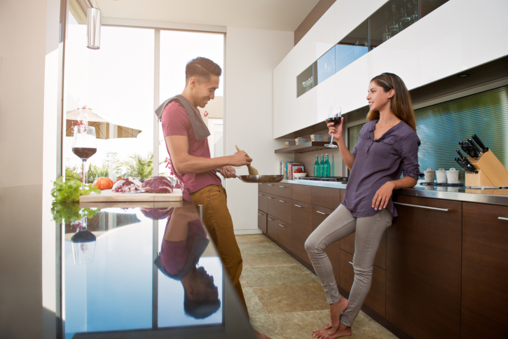 Couple chatting and drinking wine whilst cooking in kitchen